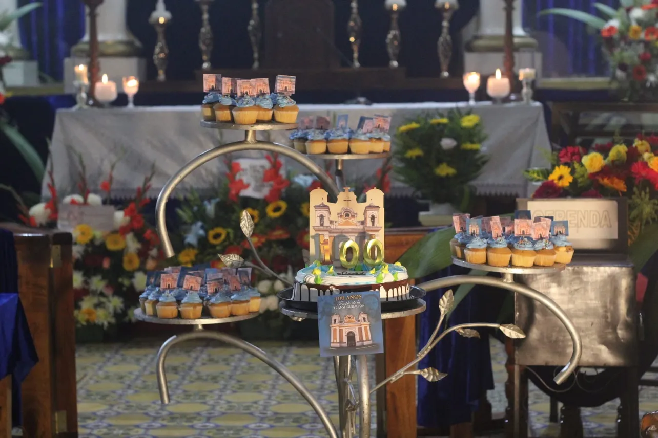 Mesa conmemorativa con el pastel de los 100 años y la silueta de las torres gemelas frente al altar mayor