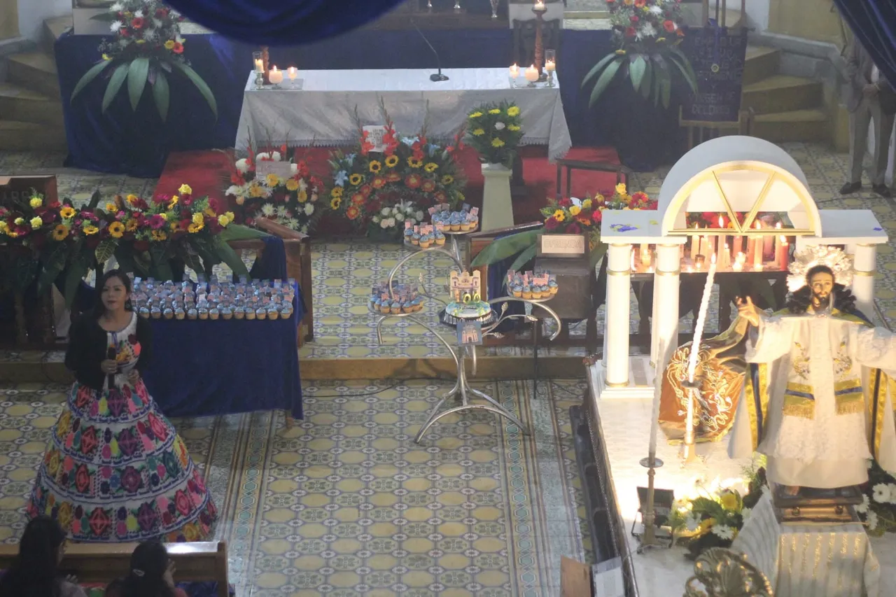 Asamblea en el presbiterio con feligresa en indumentaria tradicional quetzalteca y el anda iluminada de Jesús de la Transfiguración